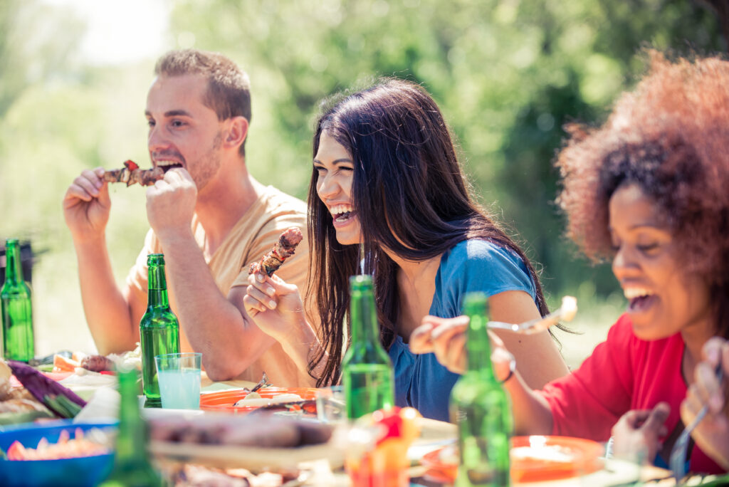 Multicultural group of friends grilling and having party in the backyard - Barbecue outdoors, people eating while talking and laughing